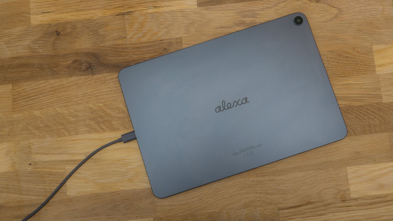 Back of the Alexa Tablet 12 Pro with the Alexa lettering and a USB-C cable plugged in, on a wooden table
