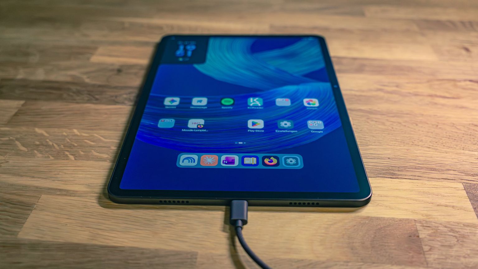 Alexa Tablet 12 Pro with a cleaned-up home screen and a USB-C cable plugged in, on a wooden table