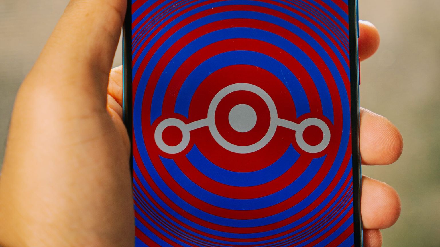 Smartphone held in hand, its screen showing the LineageOS logo over red and blue rings